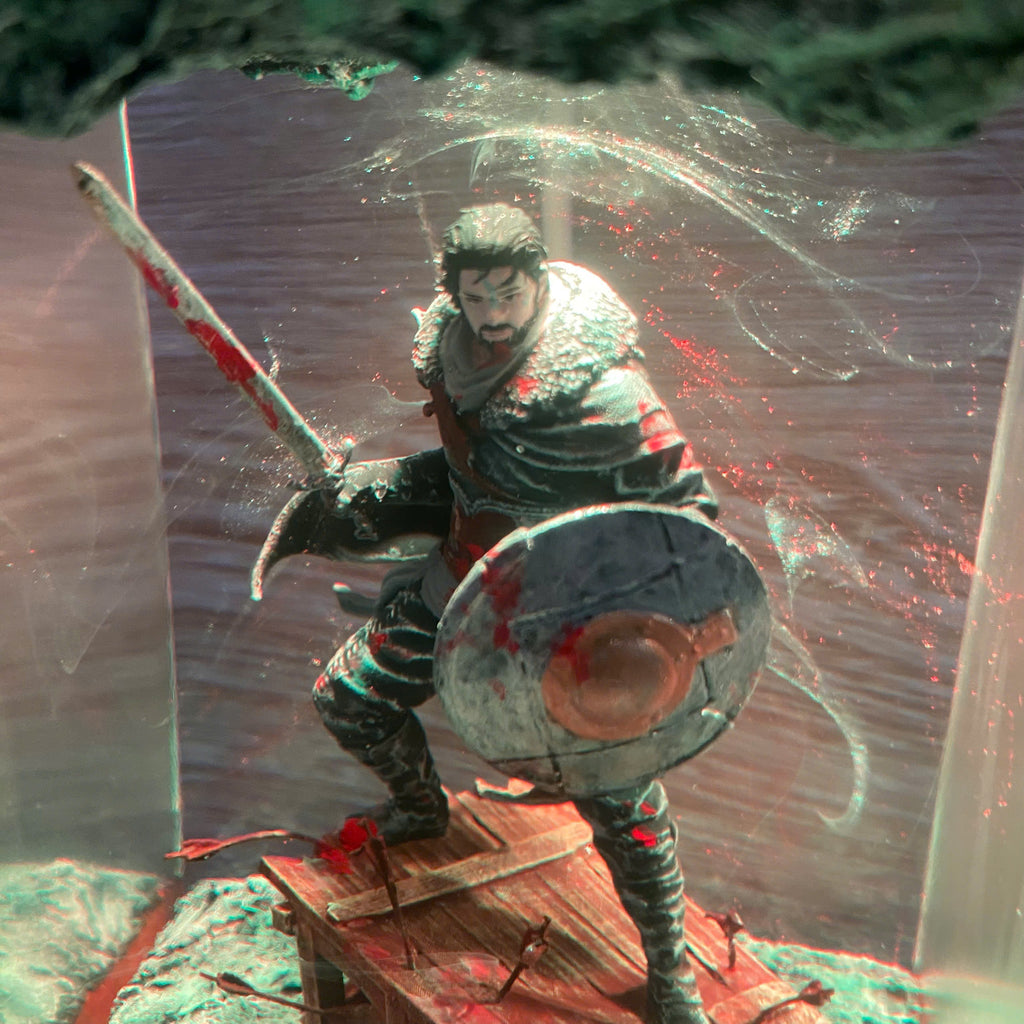 A fantasy warrior figurine or collectible statue holding a sword and round shield, posed on a wooden platform with a smoky, dramatic backdrop and red splatter details.
