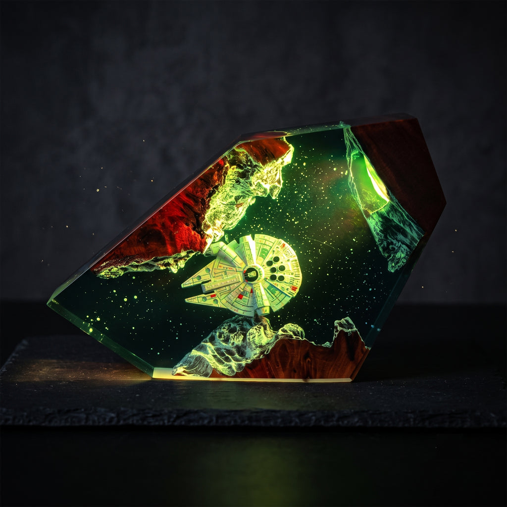 A 3D-printed geometric night light shaped like a faceted crystal, featuring a Star Wars Millennium Falcon model embedded inside green and red resin with a glowing starry space design, shown on a dark textured surface.