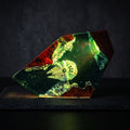 A 3D-printed geometric night light shaped like a faceted crystal, featuring a Star Wars Millennium Falcon model embedded inside green and red resin with a glowing starry space design, shown on a dark textured surface.
