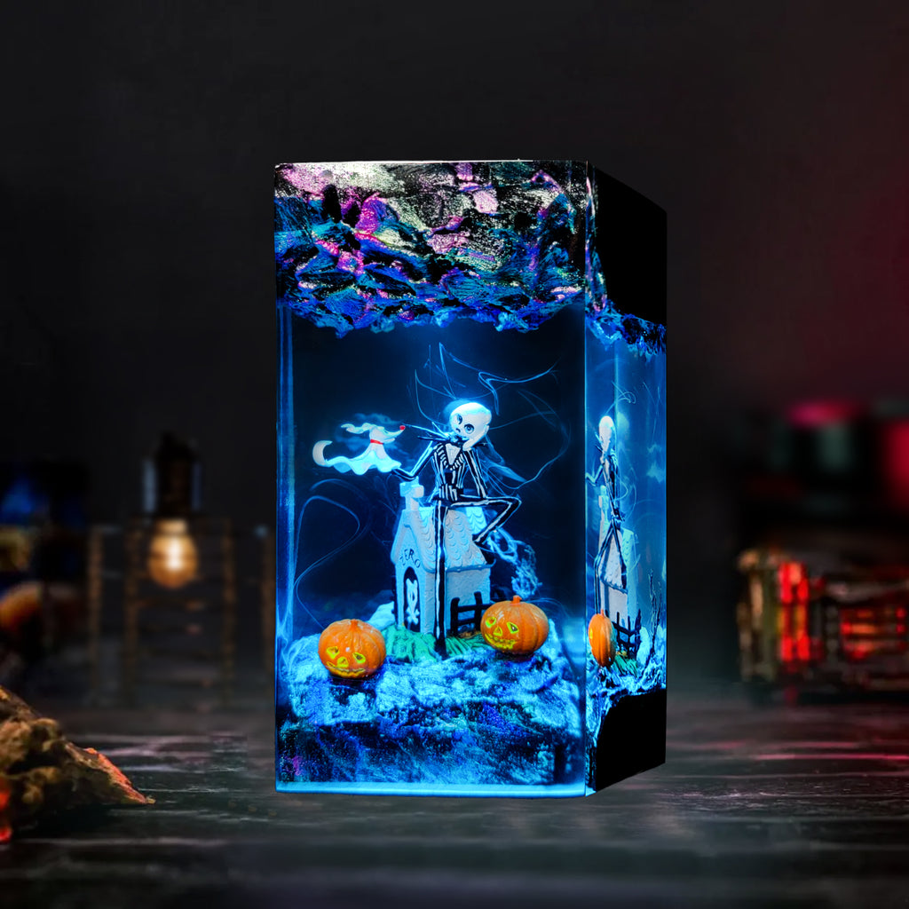 A rectangular acrylic LED light box with a Halloween theme, featuring a skeleton, haunted house, and jack-o'-lanterns glowing with blue and purple light, set against a dark, moody background.