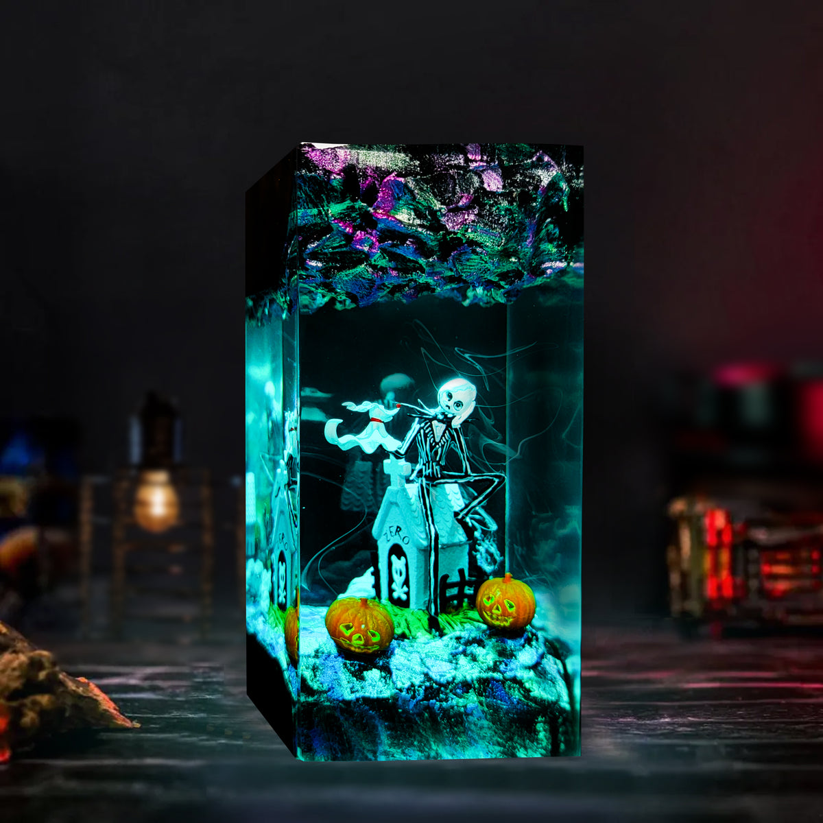 A Halloween-themed resin light box featuring a skeleton playing a violin, a haunted house, two carved jack-o'-lanterns, and a spooky forest design on the top, glowing with teal and purple light against a dark background.