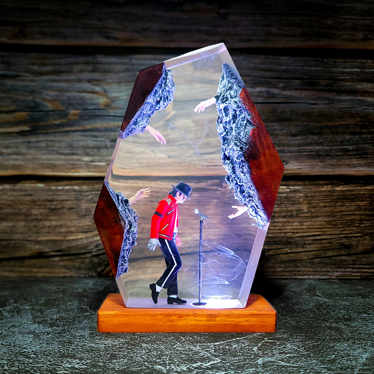 A clear resin crystal art piece featuring a miniature Michael Jackson walkie-talkie figure singing into a microphone, set on a wooden base against a rustic dark wood background.