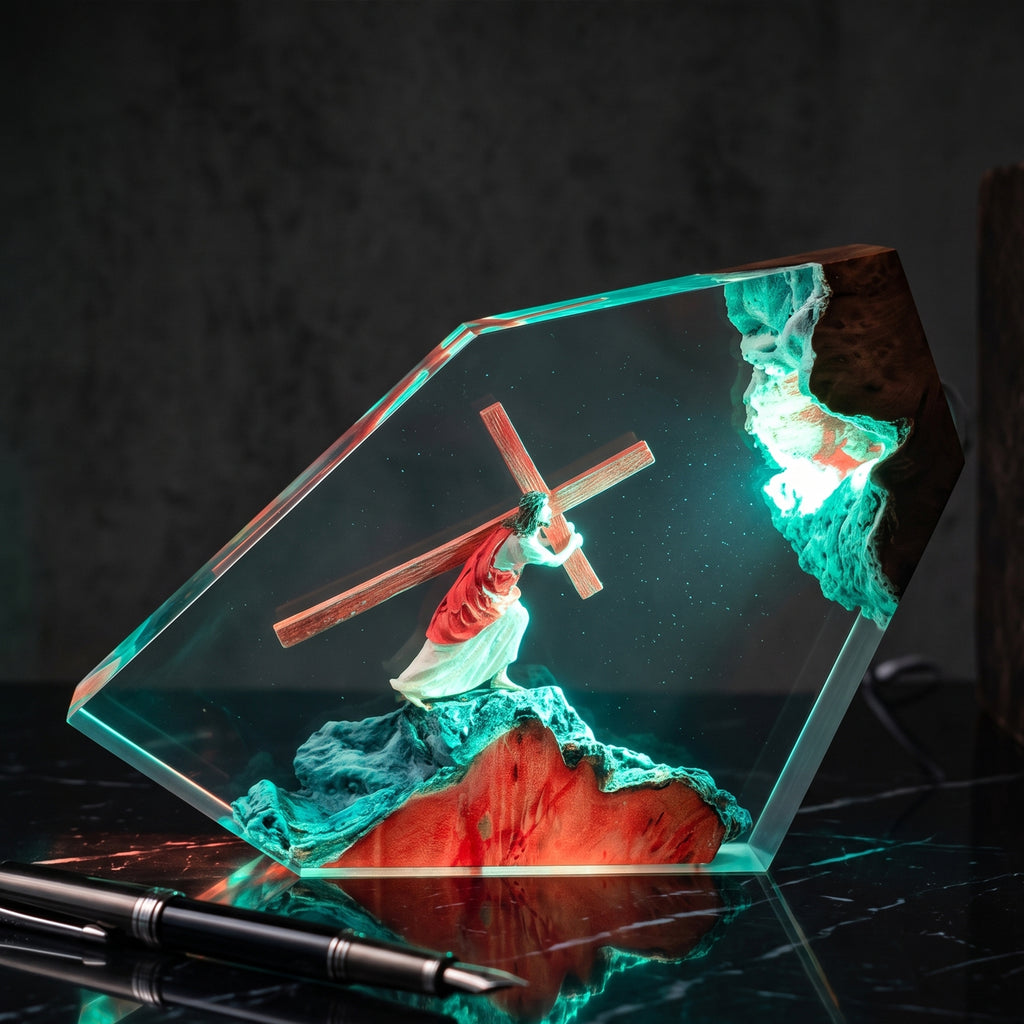 A clear acrylic crystal sculpture featuring a figurine of Jesus carrying a wooden cross, set against a dark background with dramatic green and red internal lighting.