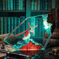 A decorative acrylic crystal lamp shaped like a mountain scene with a figure carrying a cross, shown on a dark desk with books and desk accessories in a library setting.