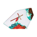 A clear resin art plaque featuring a figurine of Jesus carrying a wooden cross, set against a textured background with teal, red, and brown details, all enclosed in a geometric clear acrylic frame on a white background.