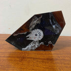 A custom resin tabletop sculpture shaped like a geometric shard, featuring a white Millennium Falcon spaceship embedded in a black starry resin, with brown wood-like swirls and white textured rock details, displayed on a wooden table against a white wall.